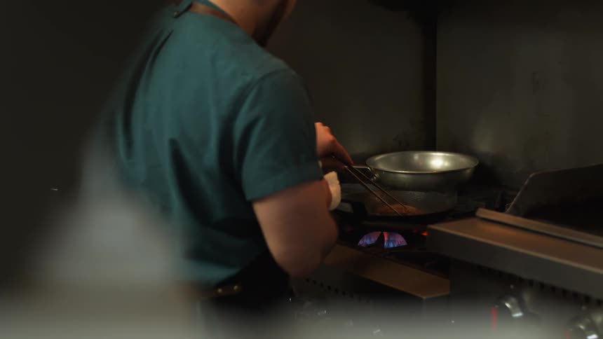 Chef cooking meat on a pan over an open fire in the restaurant kitchen