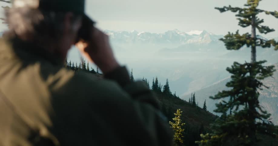 A man looking through binoculars while hiking in mountains