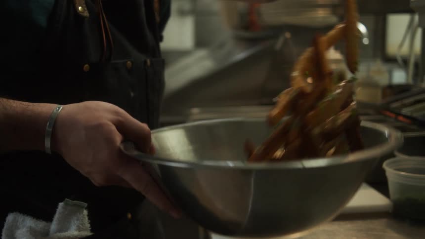 Chef tossing food on a metallic bowl in the restaurant kitchen