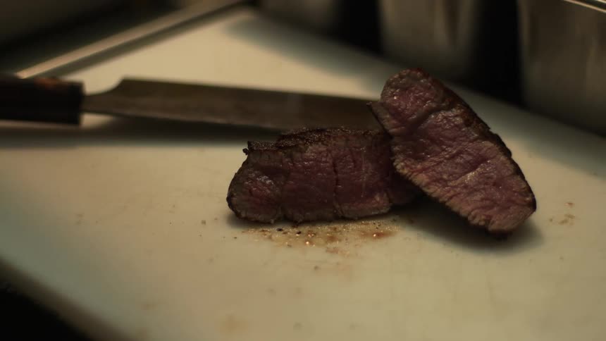 A steak sits cut in half on a cutting board in a restaurant