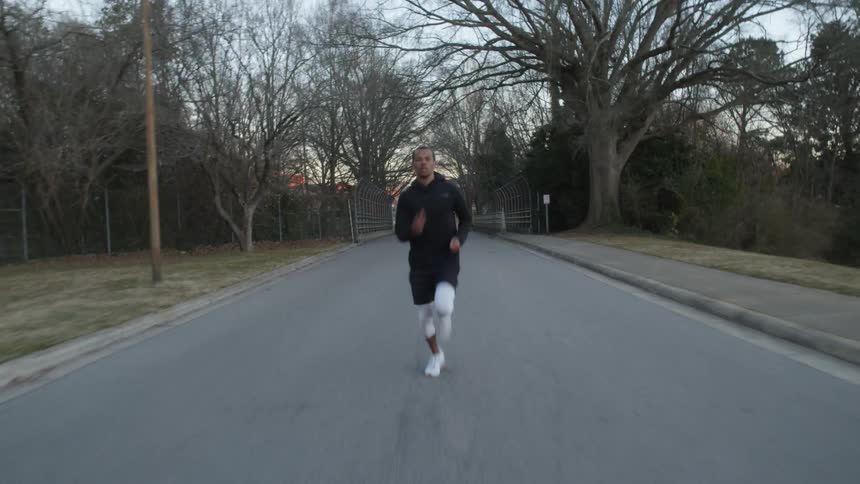 A man sprints across a pedestrian bridge and runs down the middle of the street