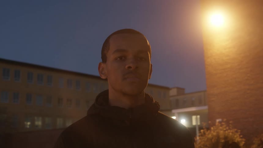 Young man standing near buildings at night looking at the camera