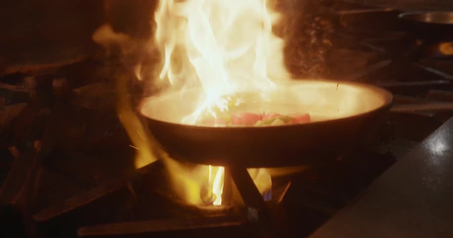 A chef cooking a pan of food over a flame on a gas stove burner