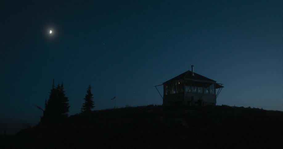 The moon shines above a small building on a hill
