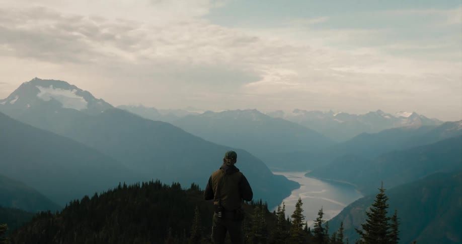 A man is standing on top of a mountain overlooking a river