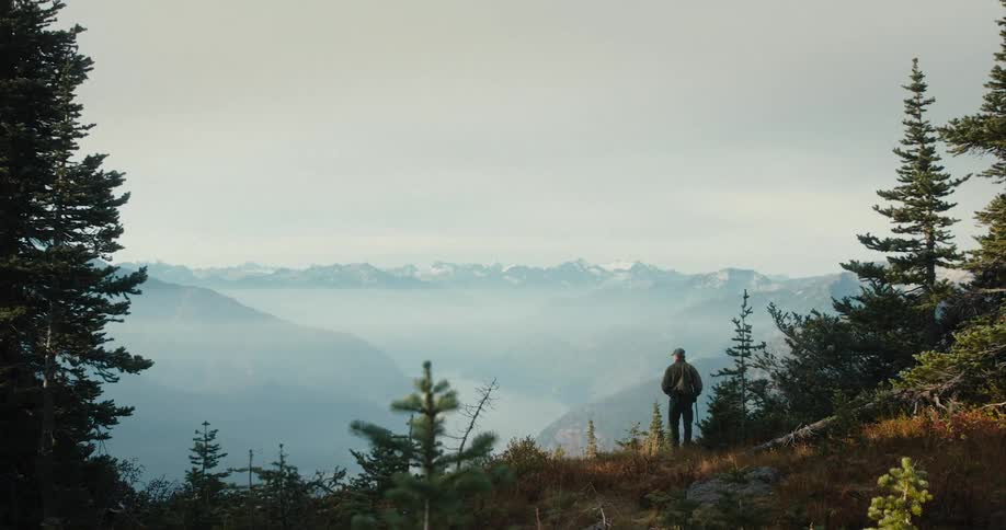 A man is walking down a steep hill and looking at a mountain range in the distance