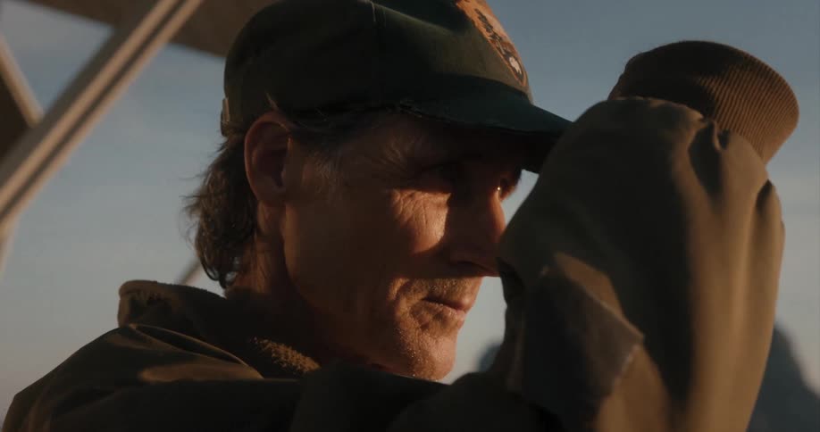 Man wearing a hat covers his eyes from the sunset sun on the mountains