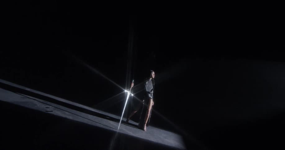 A person standing next to a reflective sword in darkness