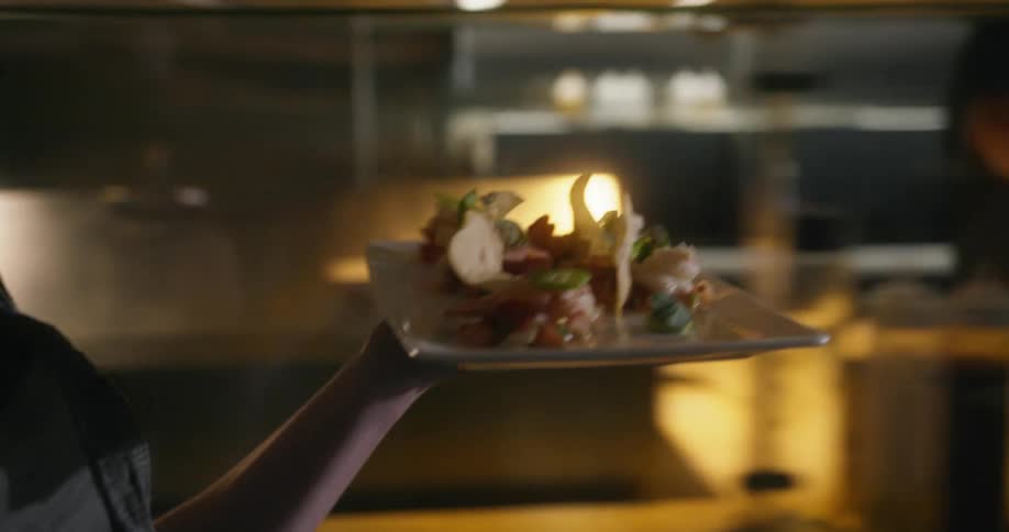 Waitress passing by workers brings a plate of food to customer in the restaurant