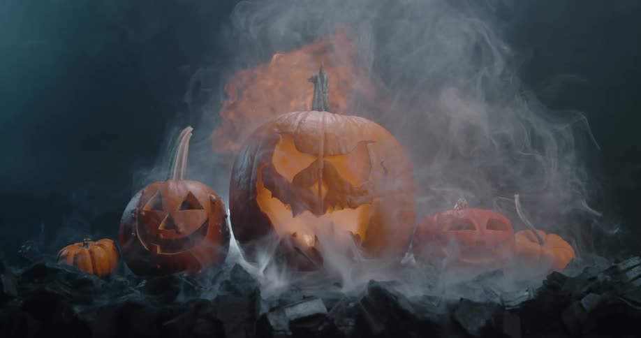 A halloween display of evil pumpkins with white and orange smoke rising in a dark studio environment