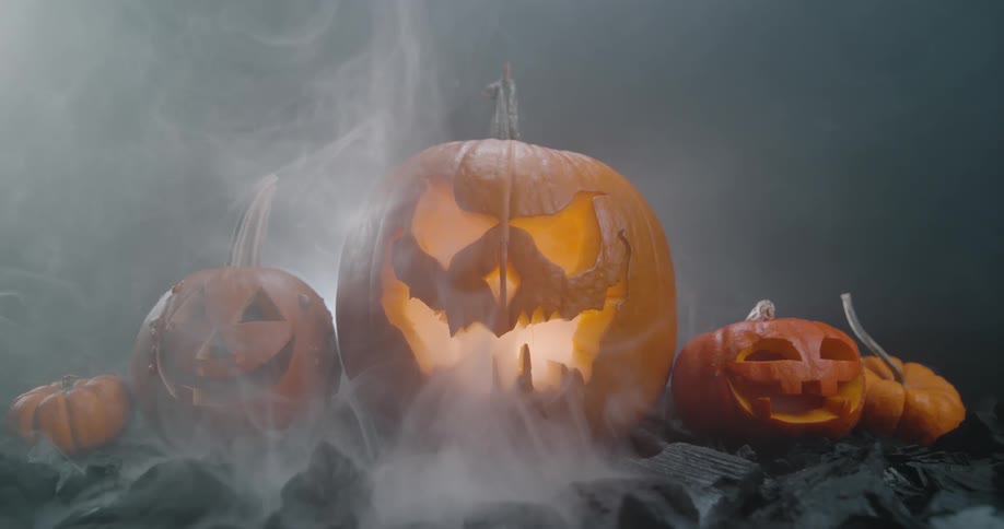 Fog rises from ground near glowing jack olantern surrounded by smaller carved pumpkins at night