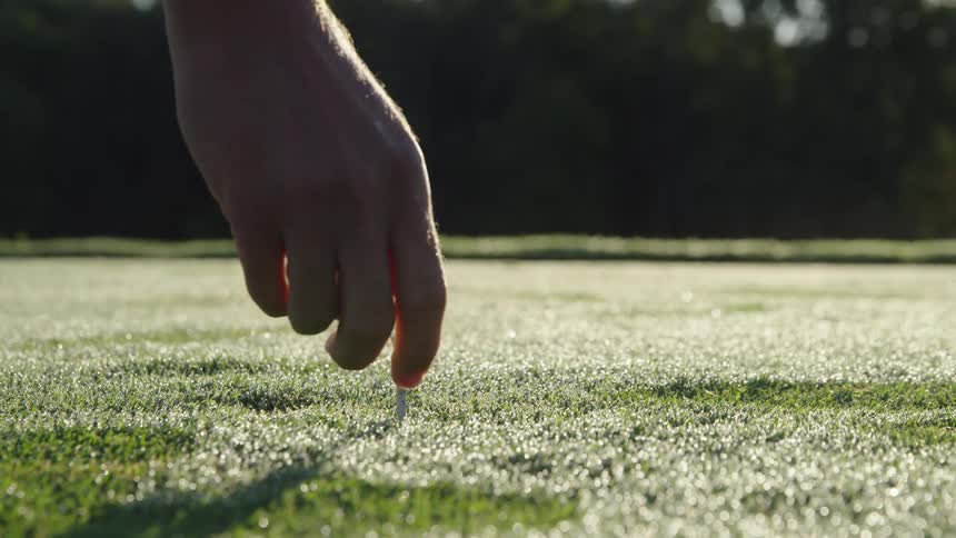 A man sets a golf ball on a tee in the grass