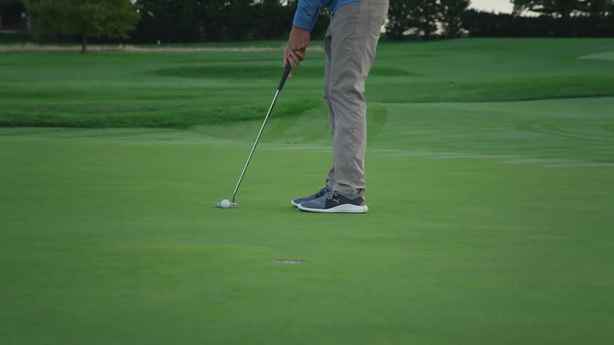 A man puts the golf ball in the hole