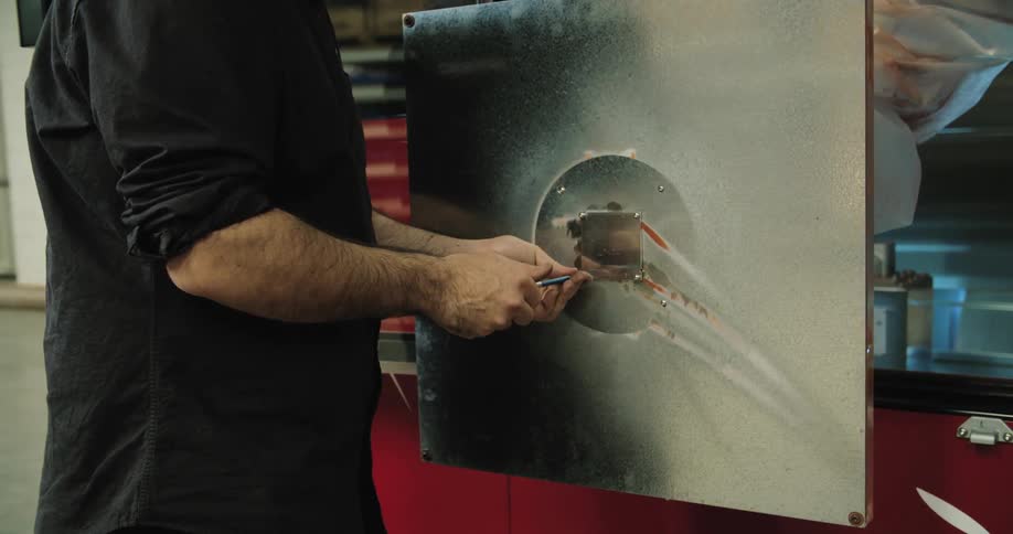 A man tightens a screw in the middle of a large metal sheet