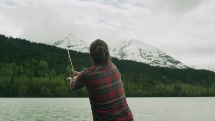 A man is fishing from a lake in the mountains