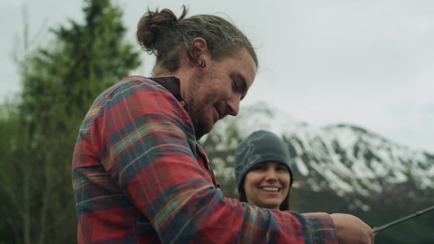 A man and woman laugh as they try to reel in a fishing rod