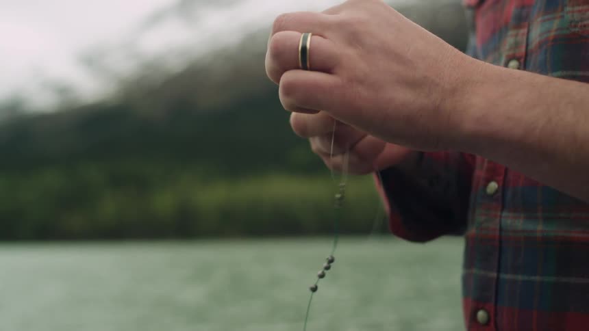 Hands tying fishing line with the lake mountain and trees behind