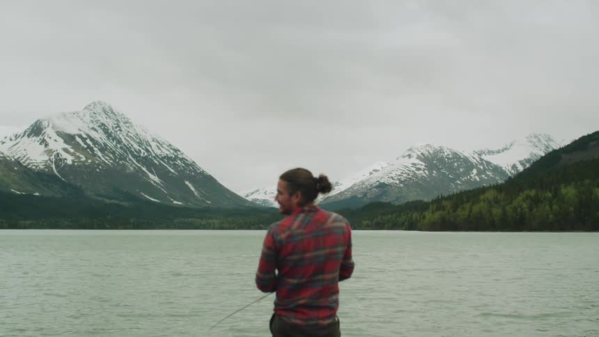 A man is fishing in the lake by the mountains