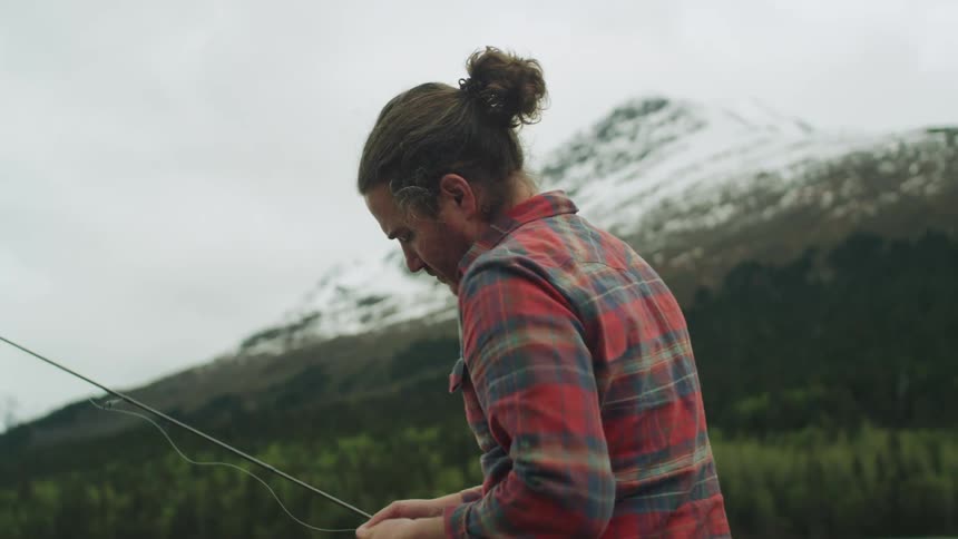 A man picks up a fishing rod and begins to windup the fishing line