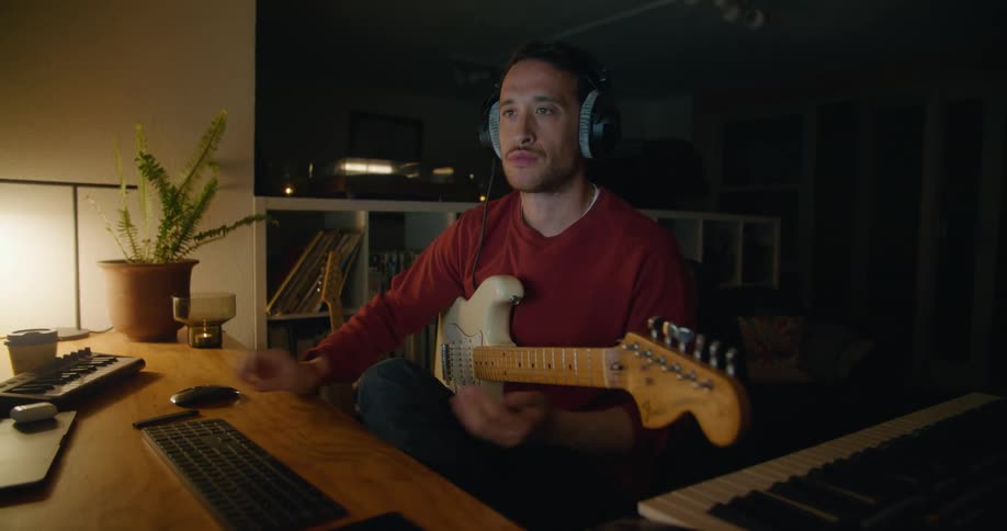 A man types on his computer while playing the guitar