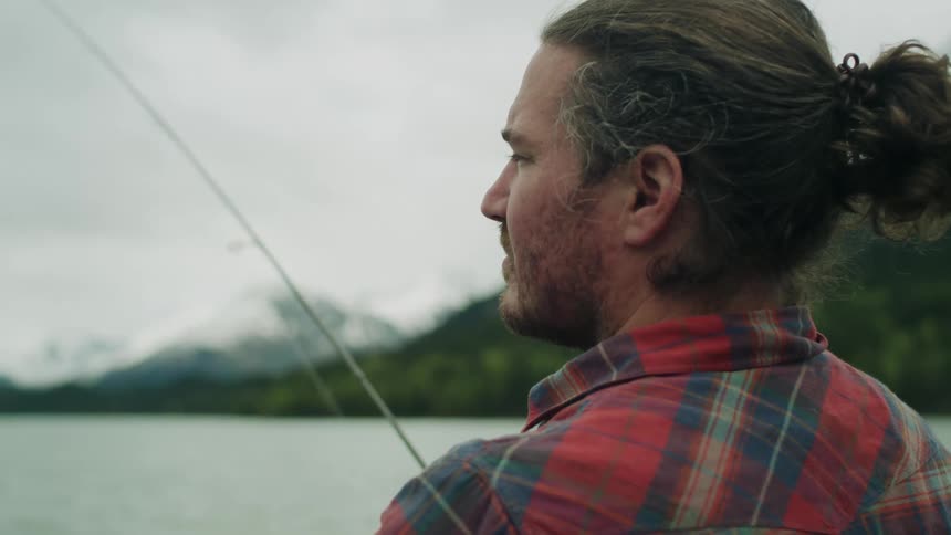A man fishes from the shore of lake in the wilderness on a cloudy day
