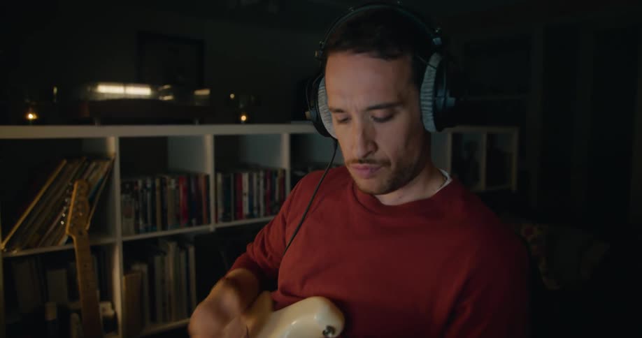 A man wearing headphones is sitting in a chair playing an electric guitar