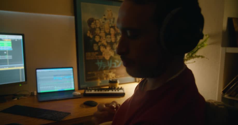 Musician playing electric guitar in front of the computers on his home studio