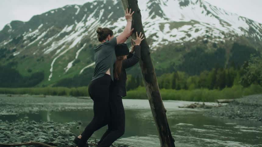 Two women pushing a log into a river