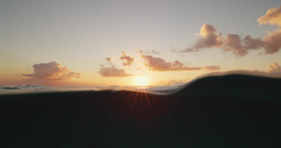 Rough ocean water moving with the sun on the horizon and clouds in the sky