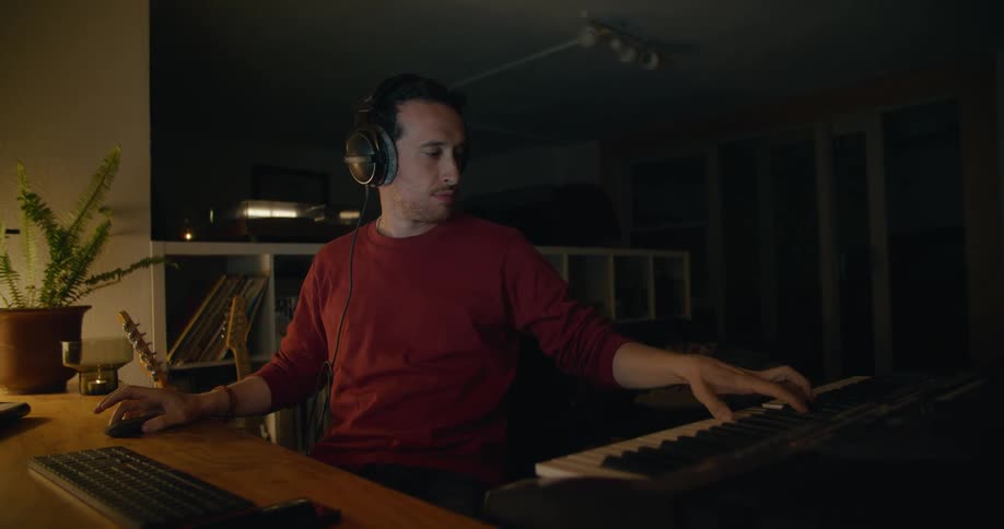A man moves back and forth between a piano and a laptop