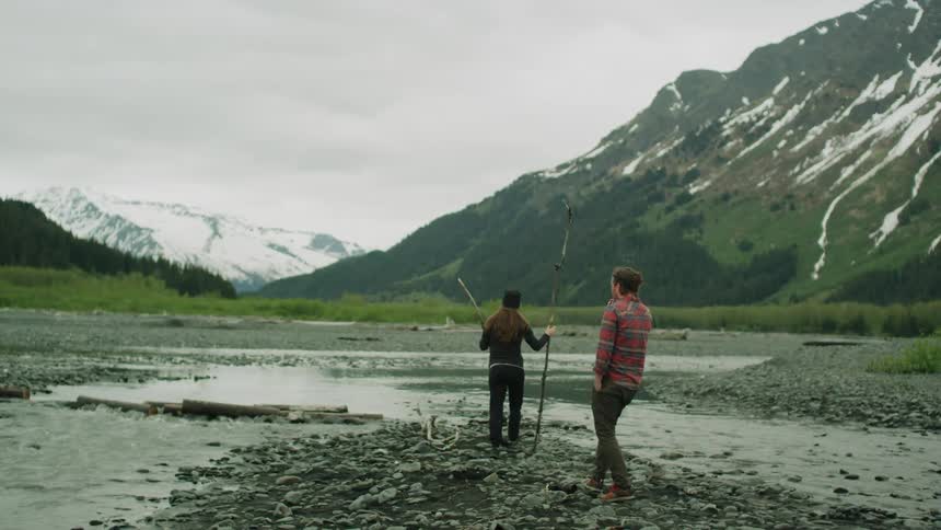 A woman picks up two sticks near the mountain range