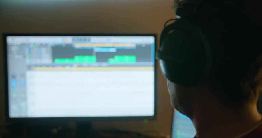 Man wearing headphones bobs his head watching digital music sheet scroll across large screen