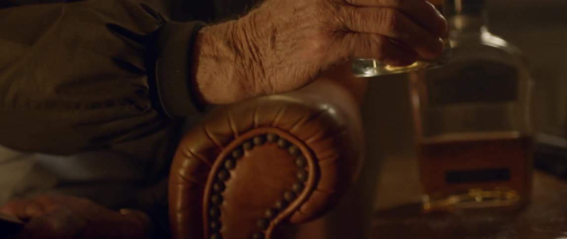 An elderly man sips a glass of liquor