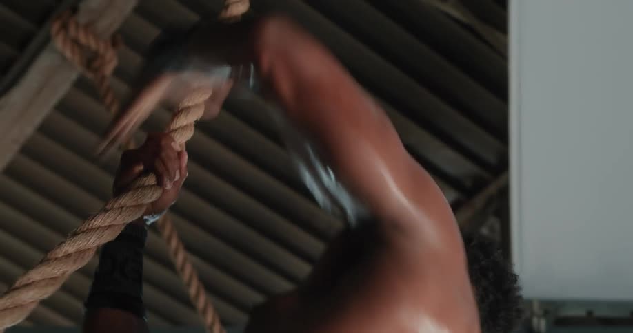 A man jumps up and grabs a rope and climbs up it as he exercises