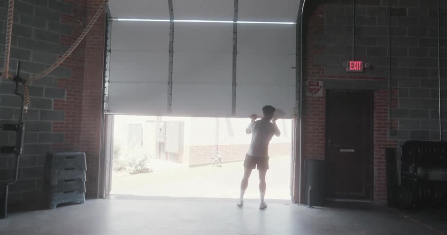 A man walks over to the garage door and opens it