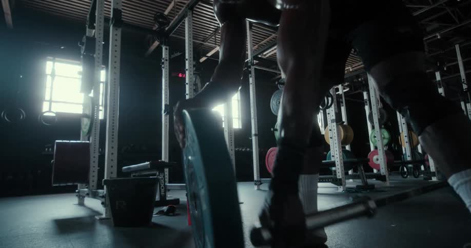 A sweating man removes a weight from a bar and carries it over to a machine
