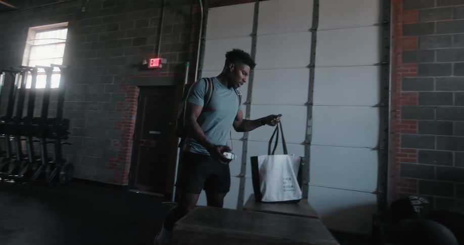 Man walks into dimly lit gym on sunny day and unzips backpack he set on flat surface