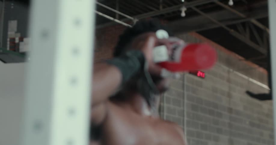 A man drinks from a water bottle as he walks toward a weight bench
