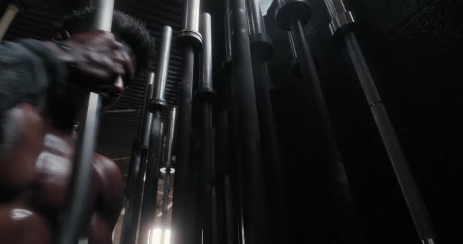 Strong shirtless muscular man picks up a bar inside a dimly lit gym