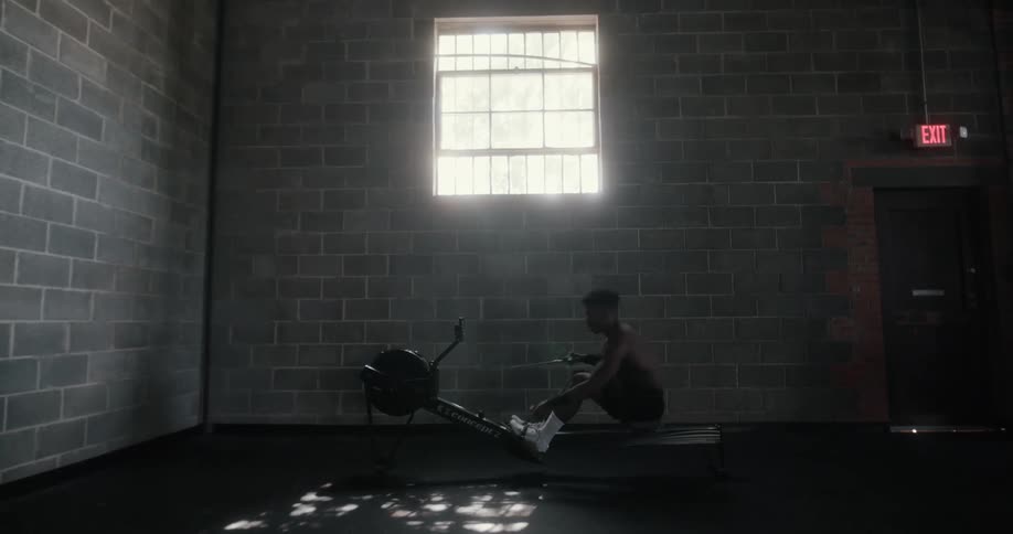 Strong muscular shirtless man working on a machine in a dimly lit gym