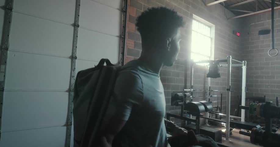 Young muscular man carrying a backpack opens a door to enter a gym