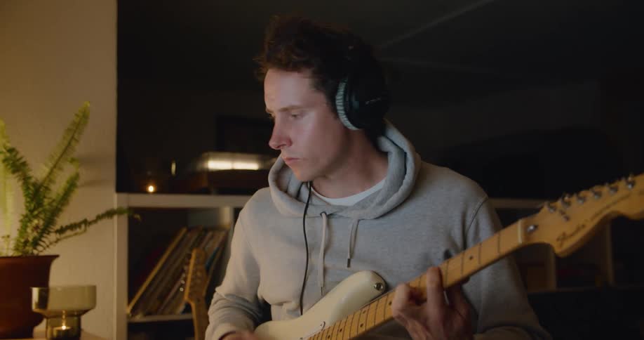 A man records himself playing guitar using audio software on his laptop