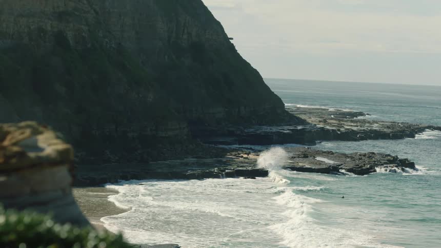Waves crash onto a beach at the foot of a mountain