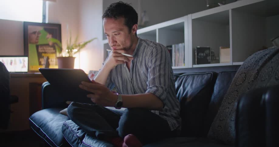 A man looks at a tablet computer while sitting on his couch
