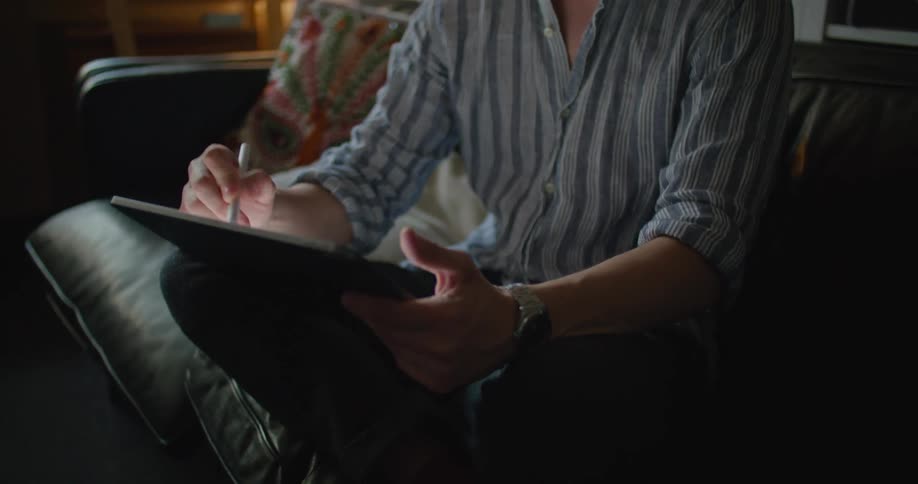 A man sits at home and writes on a tablet with a stylus