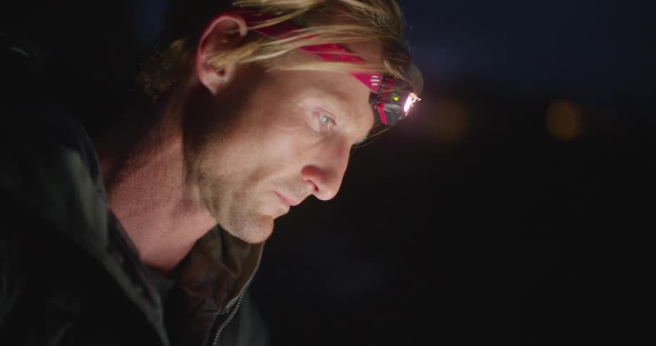 Blonde man with headlamp black coat uses tablet at night