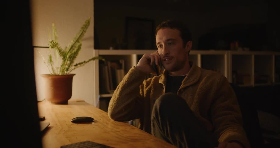 A man is sitting at a desk while talking on his cellphone
