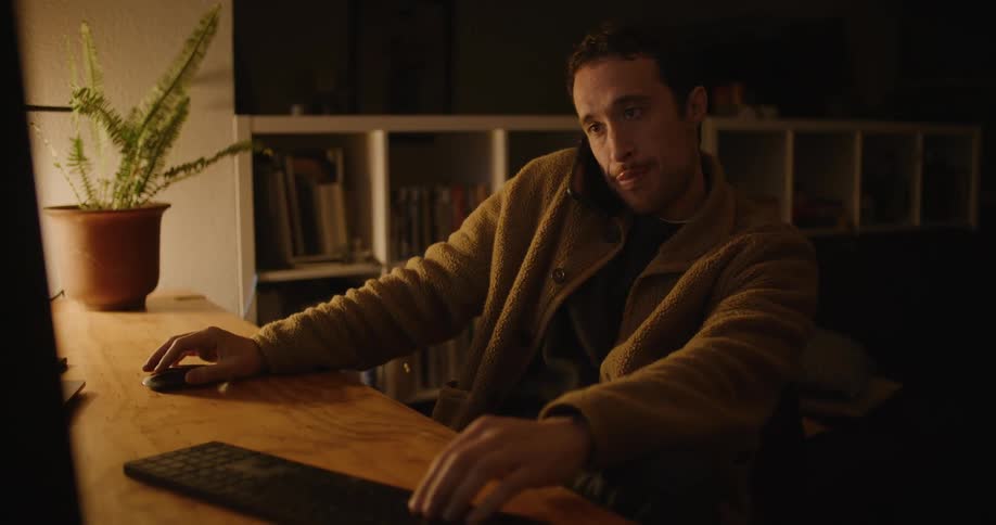 A man using a computer while talking on a smart phone