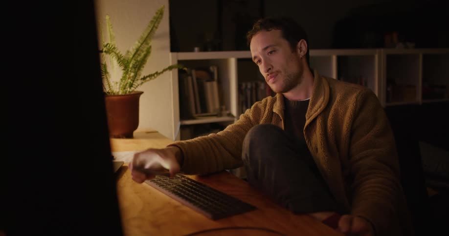 A man looks bored and tired as he looks at a screen and picks up his phone