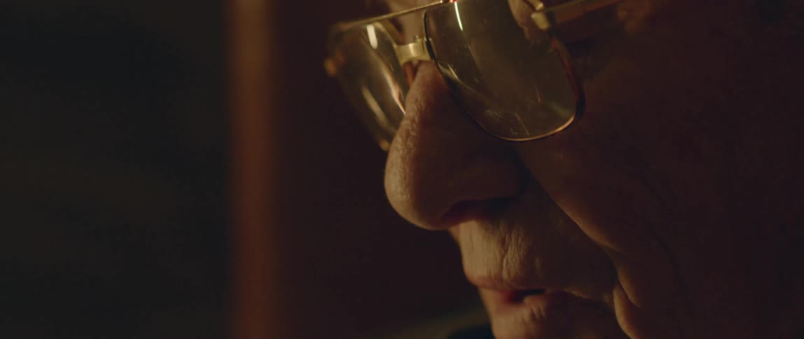 An old man wearing glasses speaking softly
